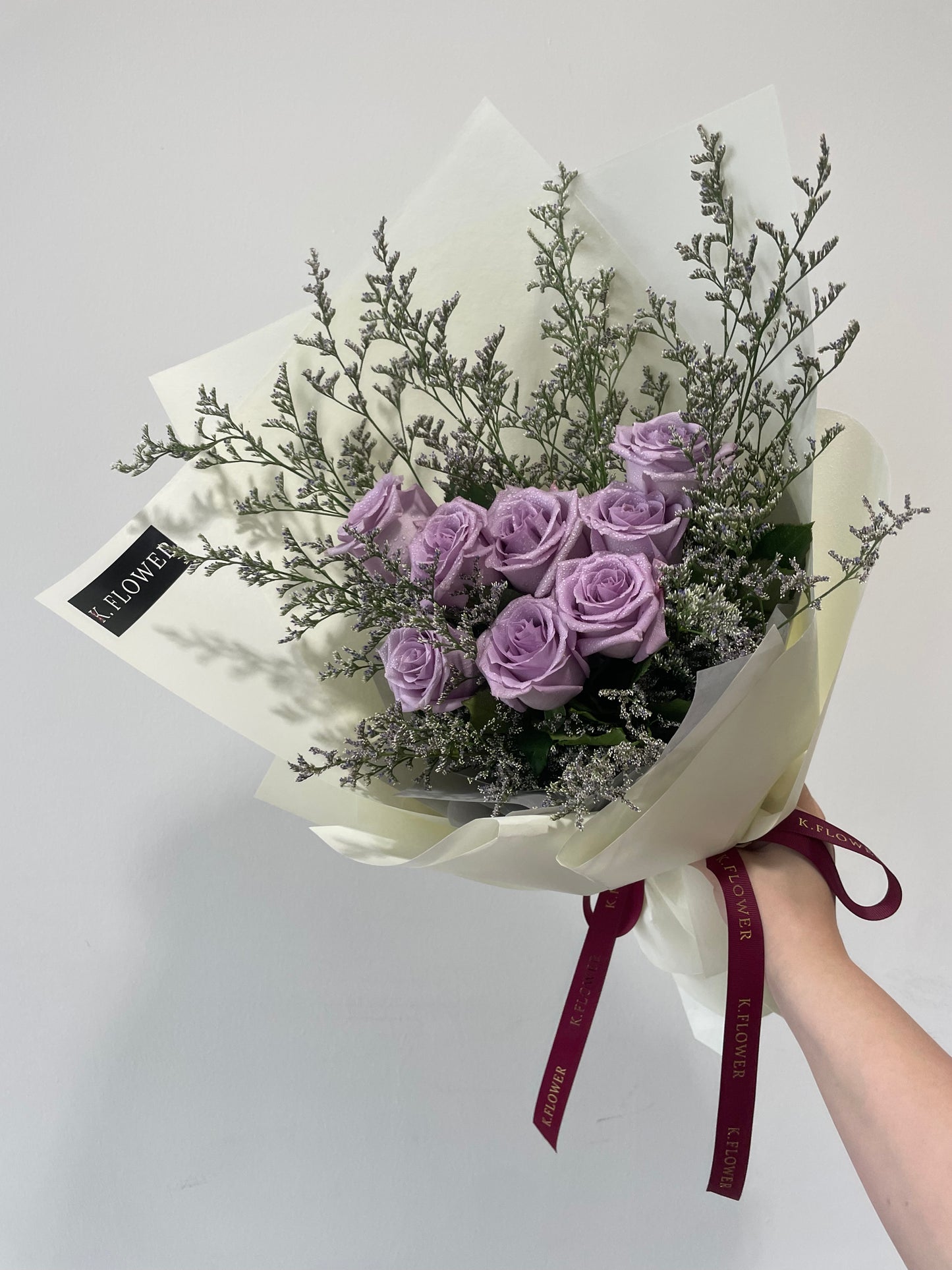 A bouquet of soft lilac roses wrapped in white paper with a decorative ribbon.